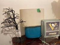 Photo of three table lamps including one with clear flower bulbs and black branches, blue and white opaque glass lamp, and Pittsburgh Penguins glass lamp