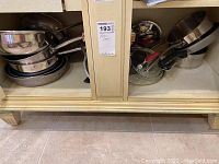 Shelf with stacked stainless steel pots, pans, and mixing bowls, including some glass lids beside them.