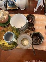 Multiple pottery items including planters, decorative bowls and small mugs in varied glazes and colors arranged on a table.