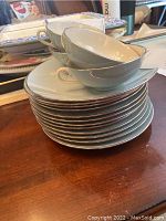 Stack of 12 salad plates with 4 coffee cups on top, showing subtle silver rim and shape of the pieces.