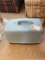Light blue plastic carrying case for Singer sewing machine with handle on top shown closed.