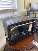 Front view of black toaster oven with glass door and silver handle on a round wooden table.