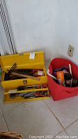 Overall shot showing yellow tool box closed next to red plastic basket containing additional tools and cleaning items on floor