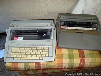 Two Brother electric typewriters GX-6750 and SX-4000 side by side on a plaid surface, showing full bodies and keys.