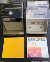 Two disk organizers containing multiple labeled and unlabeled 5.25 inch floppy disks, a yellow square item, and a Memorex disk box