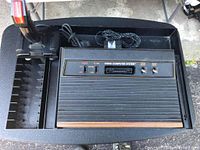 Overhead photo of Atari 2600 console, joystick controller, power supply, and cartridge organizer in a black tray