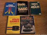 Five Atari 8-bit computer books arranged on wooden surface: Atari Graphics, Basic Atari BASIC, Computer's Third Book of Atari, Compute!'s First Book of Atari Games, Inside Atari BASIC.