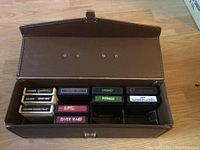 Open vintage brown vinyl carrying case with 13 Atari 2600 and Coleco game cartridges arranged in compartments.
