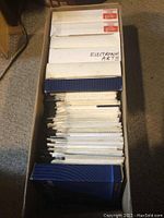 Open cardboard box filled with stacks of floppy disk envelopes and boxes labeled Electronic Arts and Pinnacle
