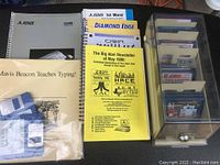 Overview of Atari 520ST manual, newsletters, typing manual, and software manual booklets with plastic box containing floppy disks on the right side.