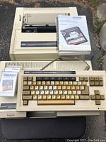 Main computer console with keyboard, printer unit, and three manuals stacked on printer, along with one software tape on keyboard.