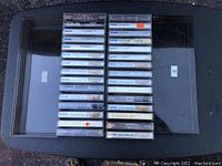 28 Coleco ADAM Digital Data Pak cassette tapes arranged in two neat rows on a black surface, visible tape labels such as 'Lorain' and 'Smart Pak'