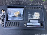 Top view of ColecoVision console with attached gray AV cable and a resealable plastic bag containing small parts placed in the cartridge slot.