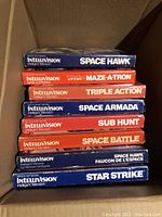 Stacked Intellivision game boxes showing titles Space Hawk, Tron Maze-A-Tron, Triple Action, Space Armada, Sub Hunt, Space Battle, and Star Strike.