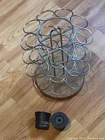 Metal Keurig pod tree holder with circular slots on a wooden surface, alongside two black reusable coffee pods with rubber seals.