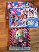 Photo showing unopened LOL Cosmetics set and two unopened Montoy 4-in-1 paper doll craft sets on wooden floor.