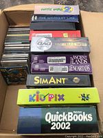 Top view of boxed PC software including Puzzle Puzz 2, The Weakest Link, Ancient Lands, Encarta 95, SimAnt, Kid Pix, and Quicken QuickBooks 2002