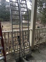 Full view of two aluminum ATV loading racks leaning against porch railing, showing tall slim frames with crossbars and s-bend shape.