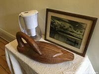 Photo showing framed vintage paddler photo, wooden goose figurine on lace-covered table, and water filter jug
