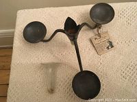 Front view of hand forged iron candle holder and removable glass vase placed next to each other on a cream knit fabric.