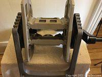 Image shows the front and bottom view of the hose reel with crank handle and base, highlighting mounting slots and handle grip.