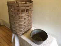 Photo showing large rattan basket with wooden base standing on a white textured fabric.