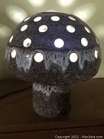 Front and side views of the mushroom lamp lit, showing light coming through the circular holes on the mushroom cap, casting patterns on the background.