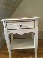 View from front showing single drawer with round knob, gold trim around the top edge, sculpted legs and bottom shelf.