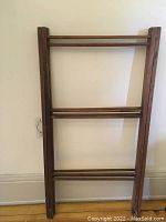 Photo showing the drying rack folded flat against a wall, clearly displaying its wooden slats and frame.