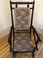 Front view showing the floral fabric seat and backrest upholstery, the wooden frame with turned spindles and arms.