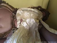 Full front view of the vintage wedding dress showing numerous buttons down the back, off-shoulder lace detailing, and pleated waist and chest area.