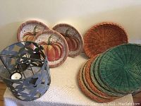 Photo showing 9 wicker plate holders of various colors and a set of paper plates with pumpkin design