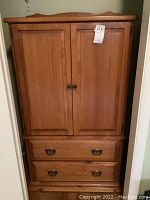 Front view of wooden armoire showing two cabinet doors above two drawers with metal handles.