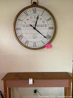 Front view of oversized round pocket-watch style clock by Howard Miller mounted on wall above wooden entry table.