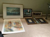 Full view of six framed art pieces arranged on floor, includes photographic print, colorful signed print, and vintage advertisements