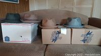 Four hats displayed on boxes on a brown couch, various woven styles and colors including black, brown, and mixed grey.