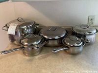 Full view of cookware set showing large stock pot with lid, sauté pan, and smaller saucepans with lids and handles on countertop.