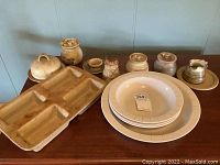 Overview of large rectangular divided serving tray, white ceramic bowls, and several smaller hand made ceramic containers on wooden surface.