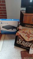 Two boxed items displayed side by side: PS4 console box and Scrabble Deluxe Edition box