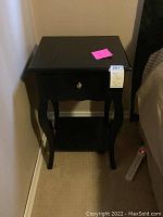Front view of black wooden side table with single drawer, decorative curved legs, and lower open shelf.