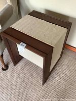 Photo of one side table showing the wood frame and woven textile center panel on carpet floor next to couch.