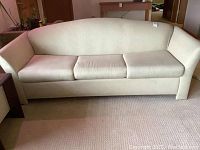 Front view of a beige upholstered sofa with three seat cushions and a straight backrest.