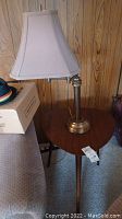 Full view of the triangle-shaped side table with the integrated brass lamp and beige lamp shade.