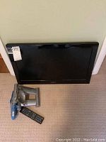 Insignia 26-inch LED TV with remote and wall mount bracket on beige carpeted floor.