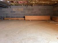 Wide shot of crawlspace floor with stacks of pine boards along wall.