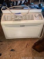 Front view of white Haier window air conditioner showing grille and control panel with power cord.