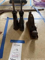 Photo showing three antique tools: two metal stamps with vertical handles and a wooden hand planer with a curved handle knob.