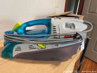 Dirt Devil spot scrubber vacuum cleaner with cord wrapped around handle, sitting on wooden surface.