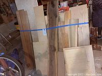 Wide view of the assortment of lumber and wood slabs secured with blue strap, showing variation in wood types and sizes.