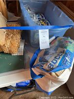 Photo of blue bin containing multiple K'NEX items and original packaging, decorative miniature hay bales, bocce balls in mesh bag, and number placards on table.